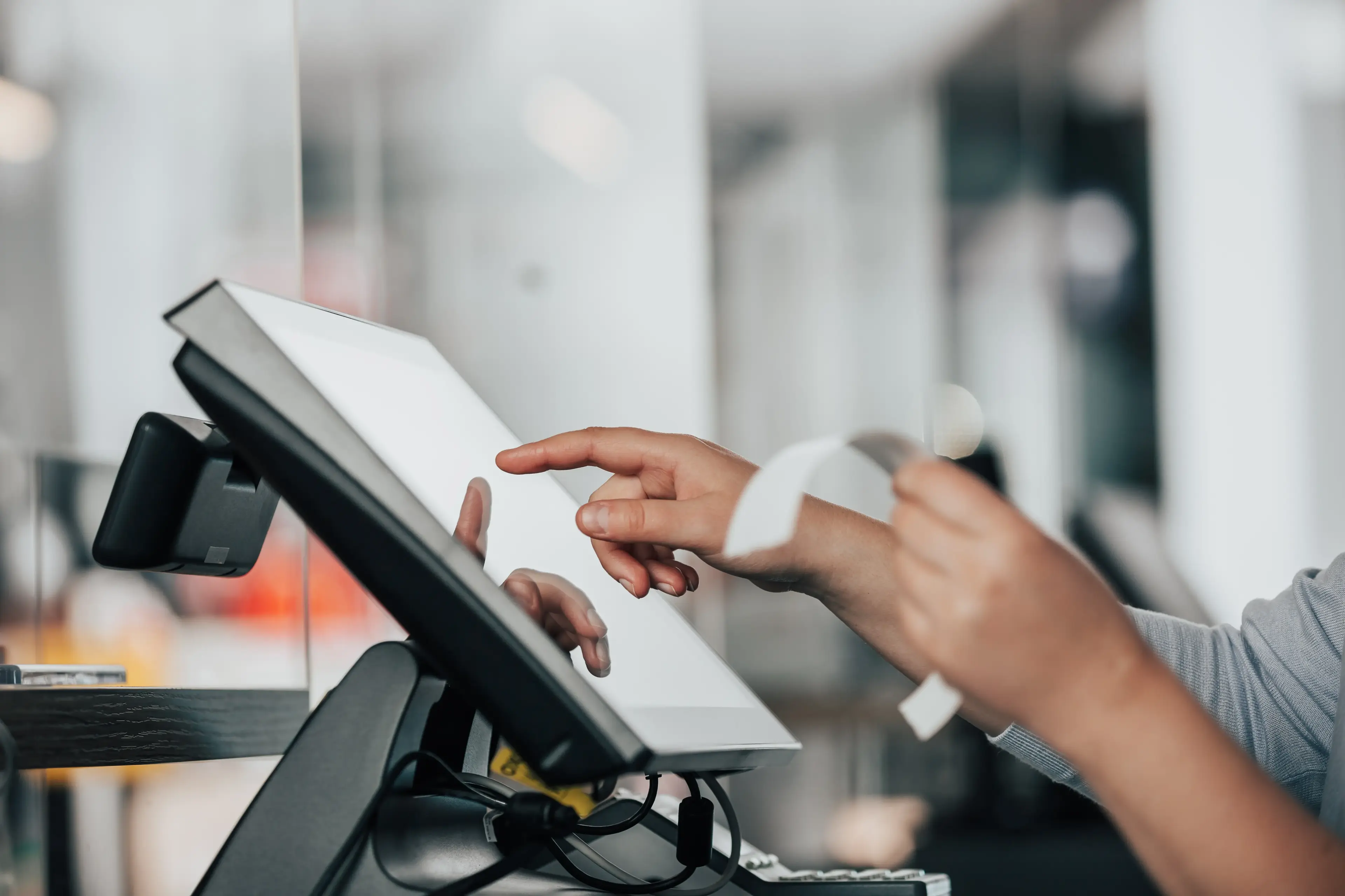 Le mani di una persona tengono una banconota di carta mentre digitano su uno schermo POS.