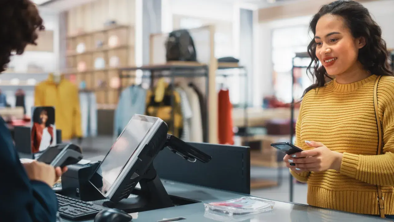 A shopper paying at a clothing store checkout while the cashier uses a point-of-sale terminal