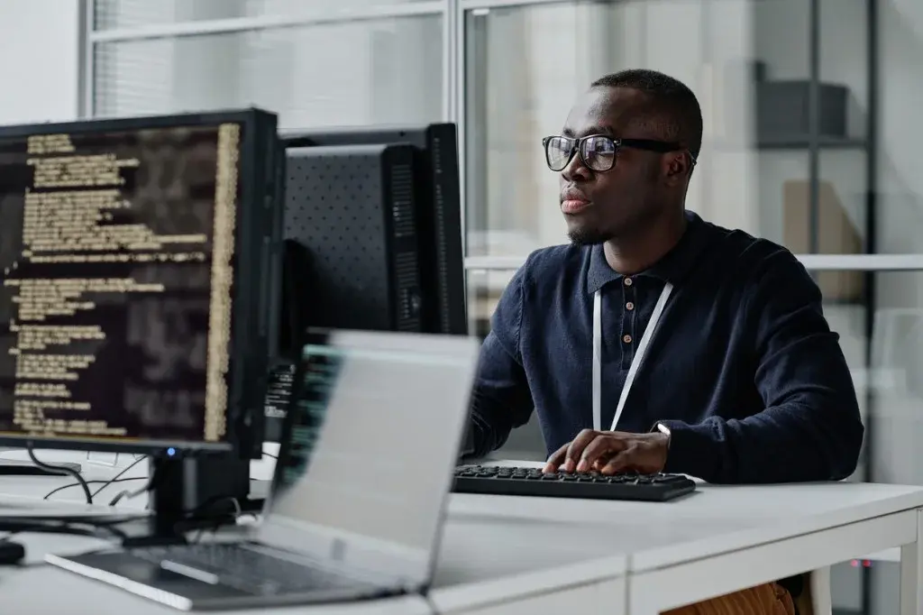 Sviluppatore software al lavoro su monitor doppi con codice in un ufficio moderno