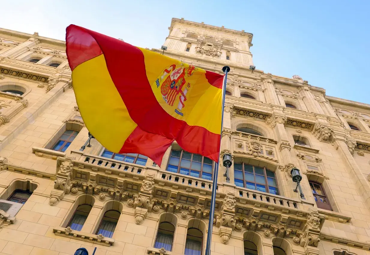Spanish flag flying in front of an ornate historic stone building