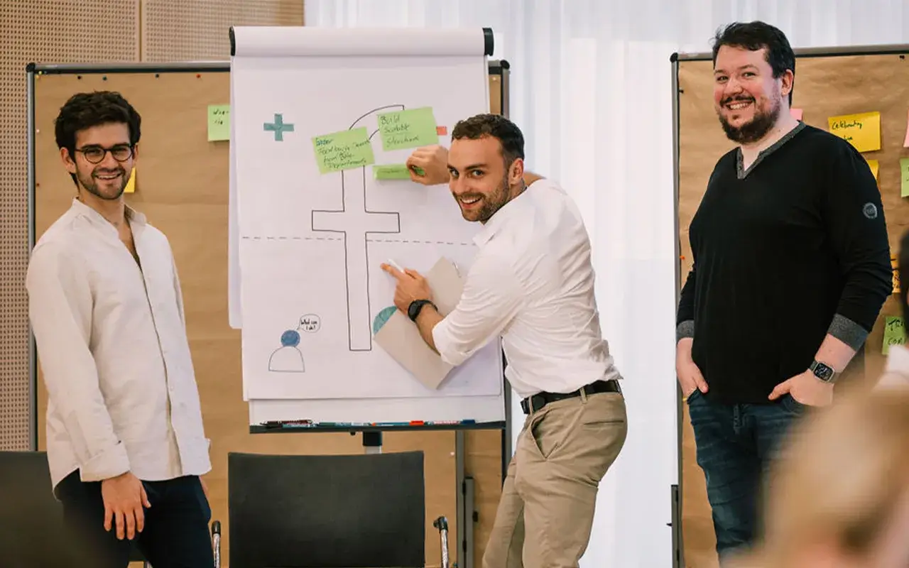 tres personas del equipo de fiskaly frente a una pizarra en un taller interactivo